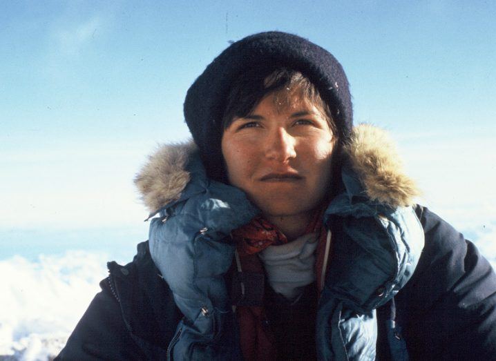 Arlene Blum dressed in layers of coats against a bright sky while mountaineering.