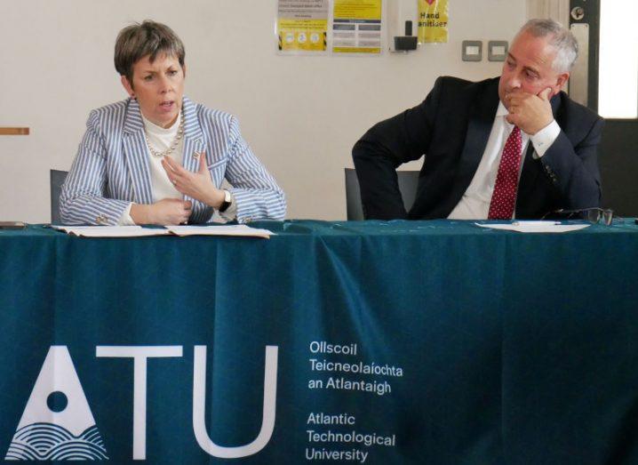 Orla Flynn and Brendan McCormack sitting at a desk draped in an ATU logo flag in dark blue.