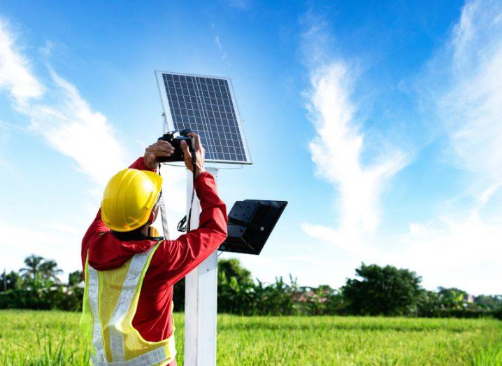 Person wearing a helmet and high-vis vest working on a solar panel in a field.