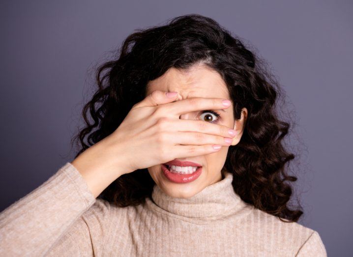 Nervous woman covering her eyes with her hand. One eye is visible though a gap between her fingers.