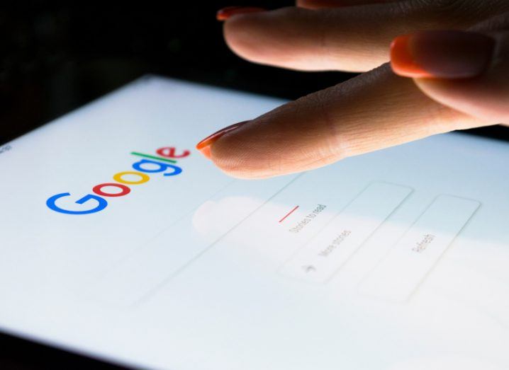 Close-up of a person's index finger touch a smartphone screen with the Google search bar displayed.