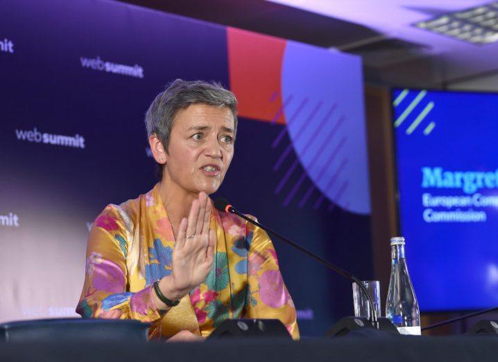 EU commissioner for competition Margrethe Vestager in 2018 at a Web Summit event, sitting down and speaking with her hand raised in front of a microphone.