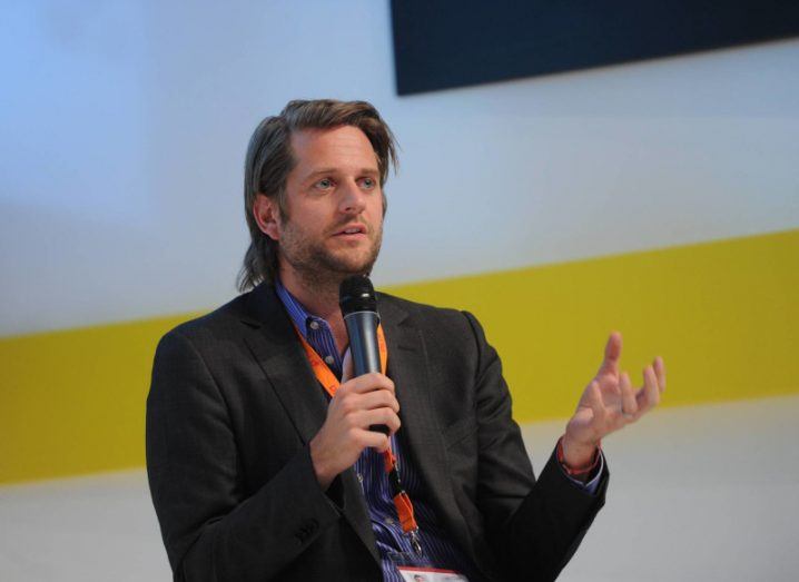 Photograph of a man in a suit jacket, speaking to an audience from a microphone while sitting on a chair. He is Klarna CEO Sebastian Siemiatkowski.