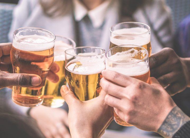 Group of people raising pints of beer in a cheers, clinking glasses together.