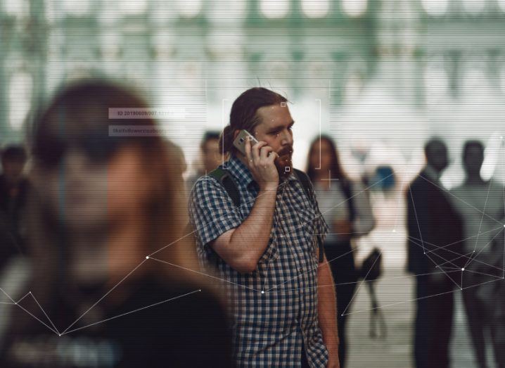 Man on the phone in a crowd with information being listed around him, identifying him with facial recognition technology.