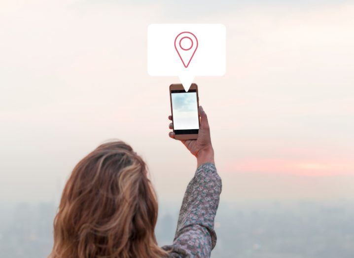 Woman holding her phone up with a location share icon above it.