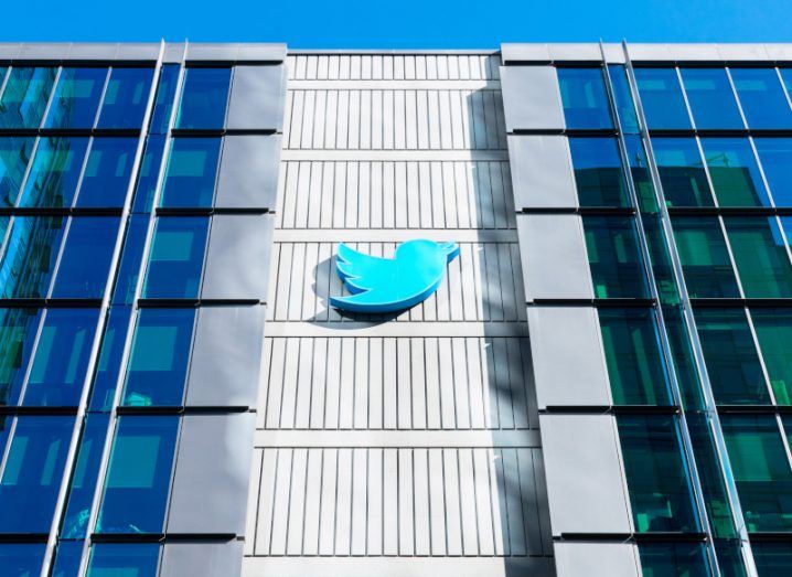 A building with the Twitter logo on the front. There are windows along the left and right of the building and a blue sky is visible above it.