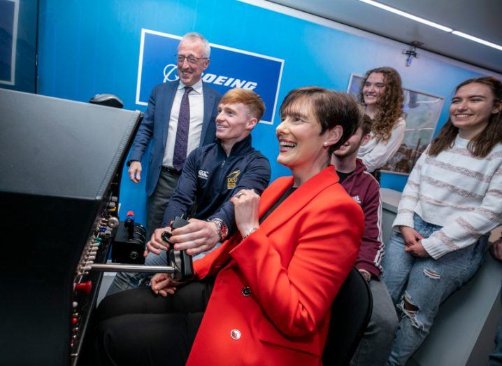 Minister for Education Norma Foley with a businessman and three teenagers standing at a flight simulator in DCU Mobile Newton Rooms.