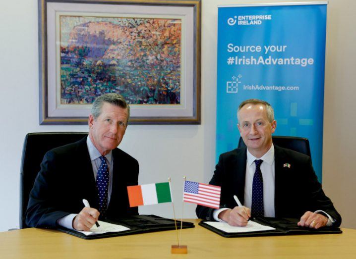 President and CEO of Texas Medical Center William McKeon and Enterprise Ireland CEO Leo Clancy sitting at a table signing papers related to a strategic partnership. An Irish flag and a US flag are on the table.