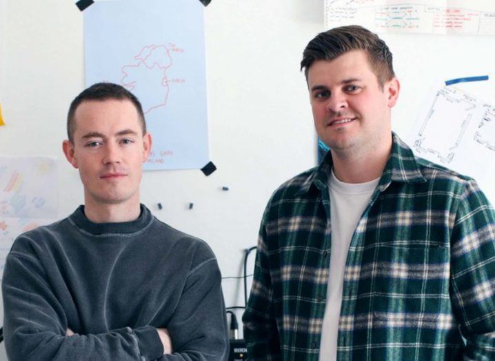 Peblo CEO and co-founder Jake Browne and Wayflyer co-founder and CFO Jack Pierse standing together in front of a white wall, that has a piece of paper taped onto it with a red drawing of the outline of Ireland.