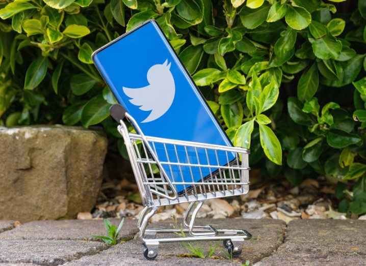 A phone in a mini shopping cart with the Twitter logo on the screen.