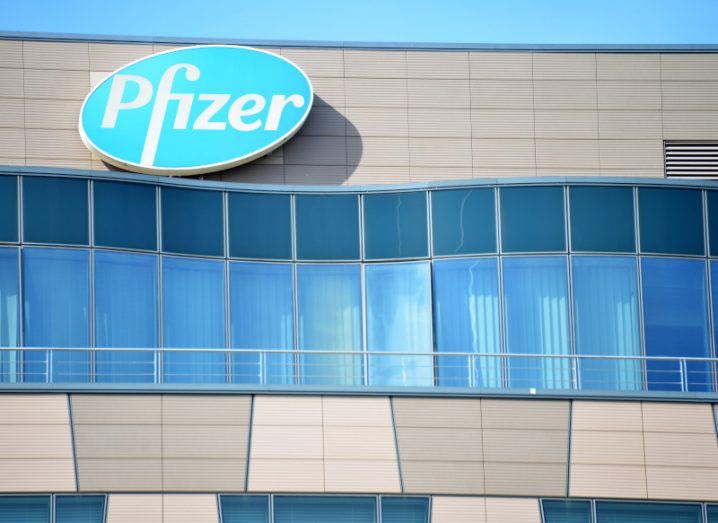The Pfizer logo in blue on a grey building with glass windows reflecting the sky.