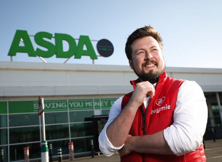 Man stares into the distance with arms folded. An Asda supermarket can be seen behind him.