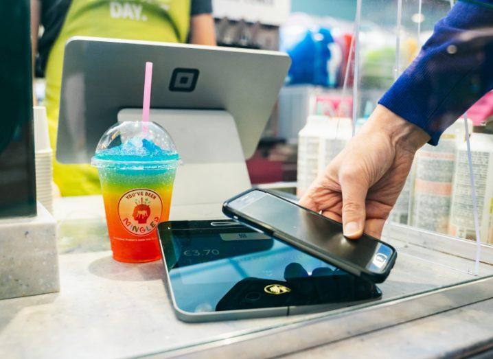 A person holding a phone close to a card payment device at a shop counter.