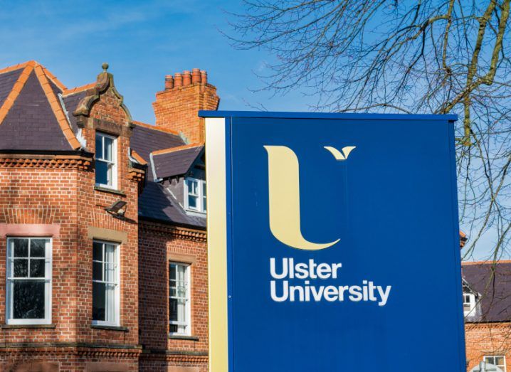 A sign that has the Ulster University name and logo on it, with a building in the background.