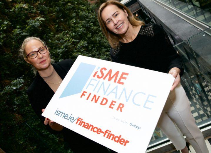 Two women hold a sign that reads ‘ISME Finance Finder’.