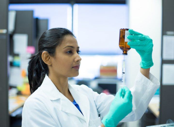 Woman in a lab coat holding a brown bottle and syringe.