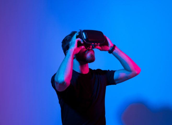 A young man in a black t-shirt wearing a virtual reality headset against a blue background.