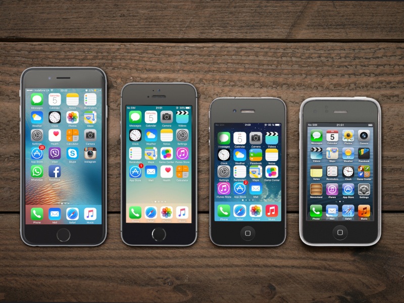 Four iPhones lined up beside each other on a table with their home screens showing.