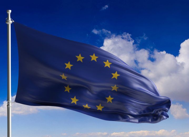 A blue EU flag waving with clouds and a blue sky in the background.