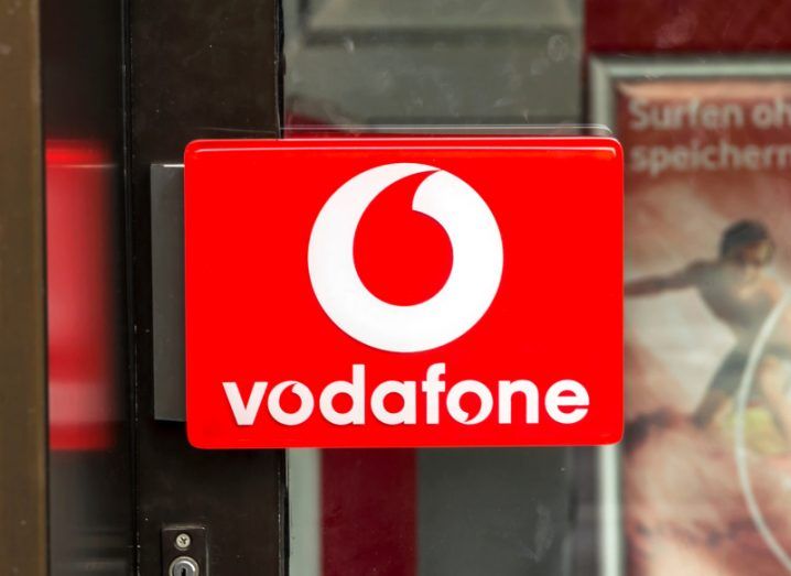 Vodafone logo on the window of a door, with a vodafone advertisement visible in the background.