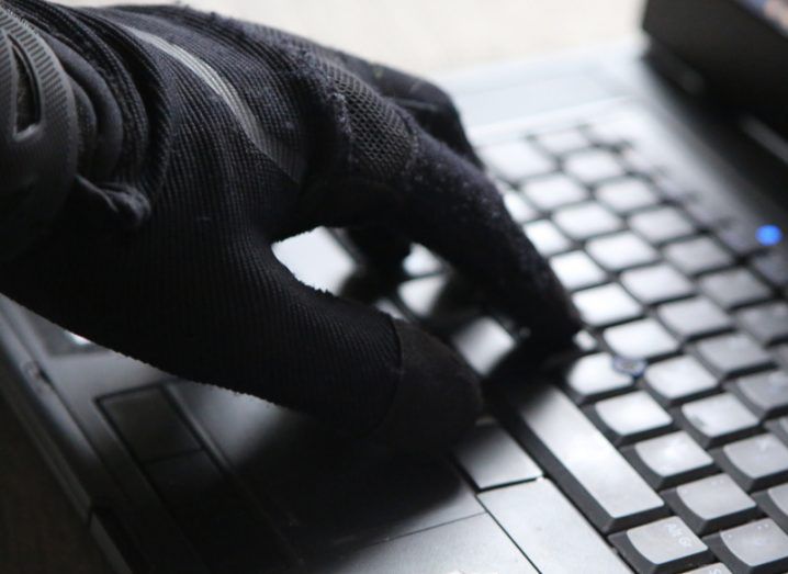 A hand wearing a black glove typing on a laptop keyboard.