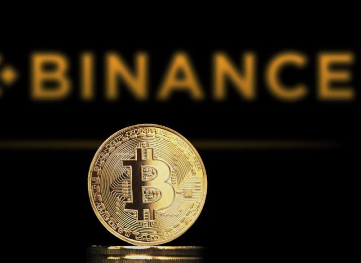 Gold bitcoin in front of the Binance logo in orange on a dark background.