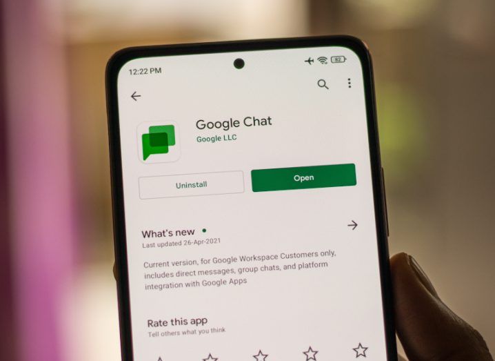 A person's hand holding a phone. On the screen is the option to open the Google Chat app.