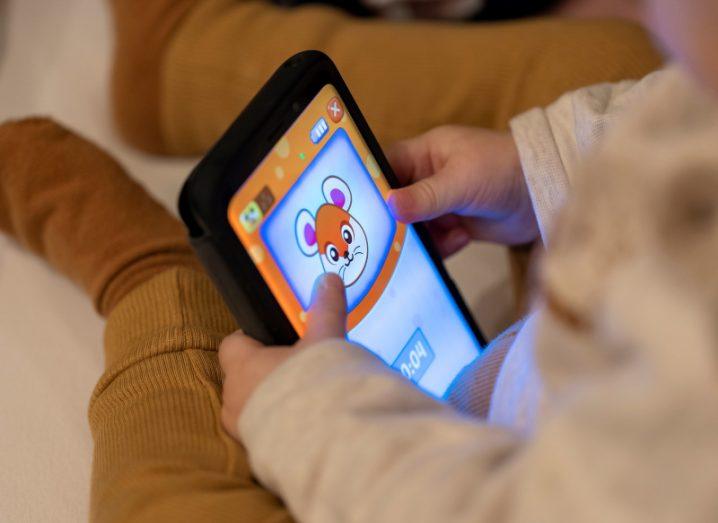 A baby holding a mobile phone that has a cartoon mouse face on the screen.
