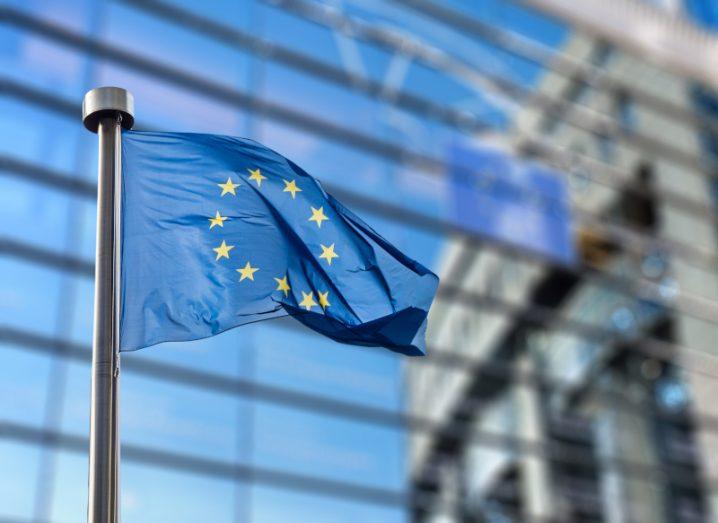 An EU flag waving in the wind against a backdrop of the EU buildings.