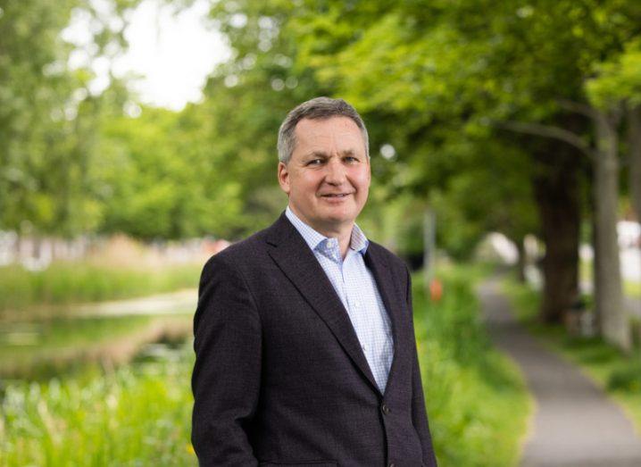 A man in a suit standing on a footpath with trees and grass in the background. He is Cathal Friel, executive chair of Open Orphan.