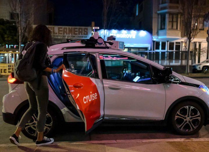 On a dark street in San Francisco, a woman opens a rear door to enter a driverless taxi branded with Cruise’s logo.