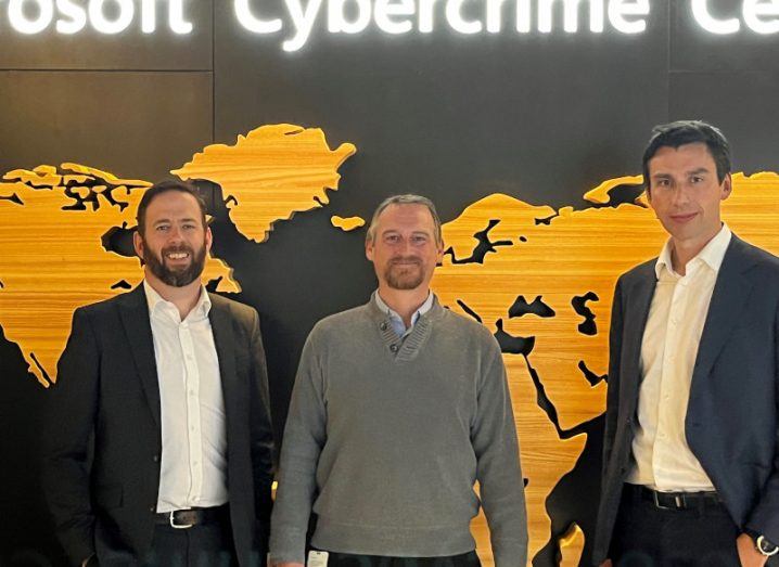 Three men standing in front of a map of the world on the wall behind them with the word cybercrime visible above them.