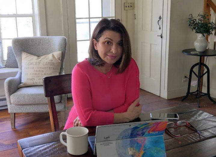 A woman wearing a pink jumper sits at a table in front of a small tablet in her house. She is smiling at the camera. She’s the CISO of Malwarebytes.