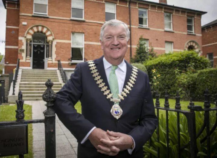 John Power, president of Engineers Ireland, standing outside a red brick building wearing a medal.
