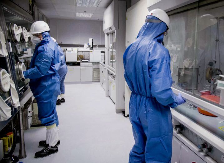 A group of workers in protective clothing complete different tasks in a pharma lab.