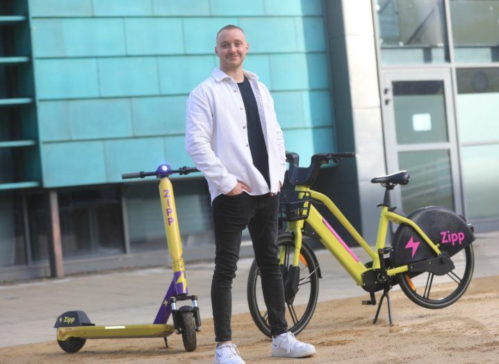 Zipp Mobility CEO and founder Charlie Gleeson stands next to a Zipp e-bike and e-scooter.