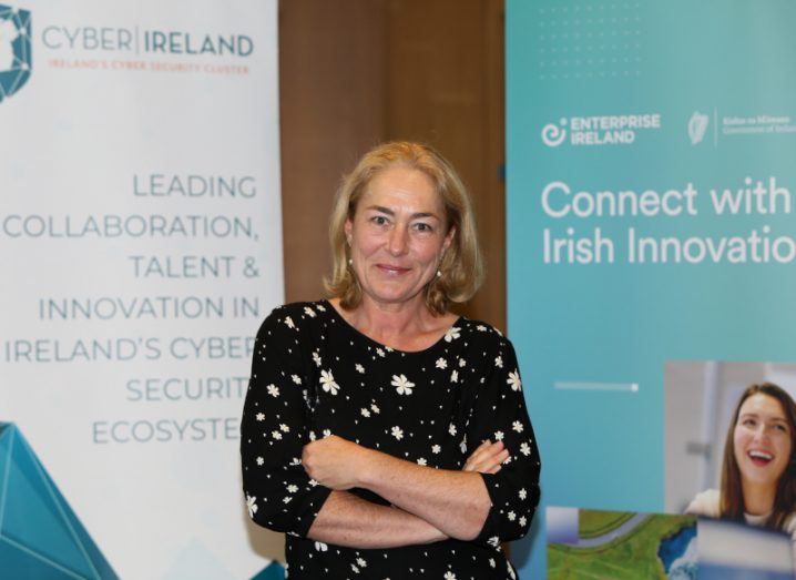 A woman stands with folded arms in front of event posters at the cybersecurity start-ups pitching event in Dublin.