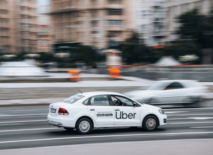 Image of a moving Uber taxi with blurred background of roads, buildings and other cars.