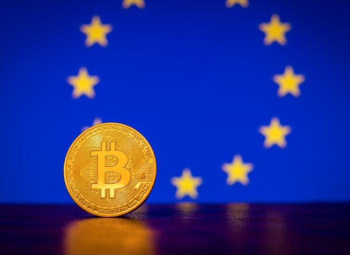 A coin with the bitcoin logo on it in front of an EU flag.