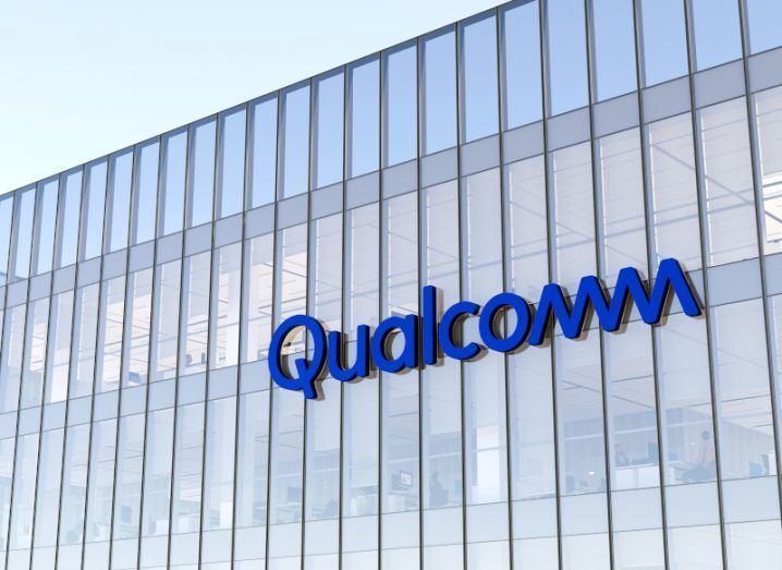 The Qualcomm logo on a glass building reflecting the sky.