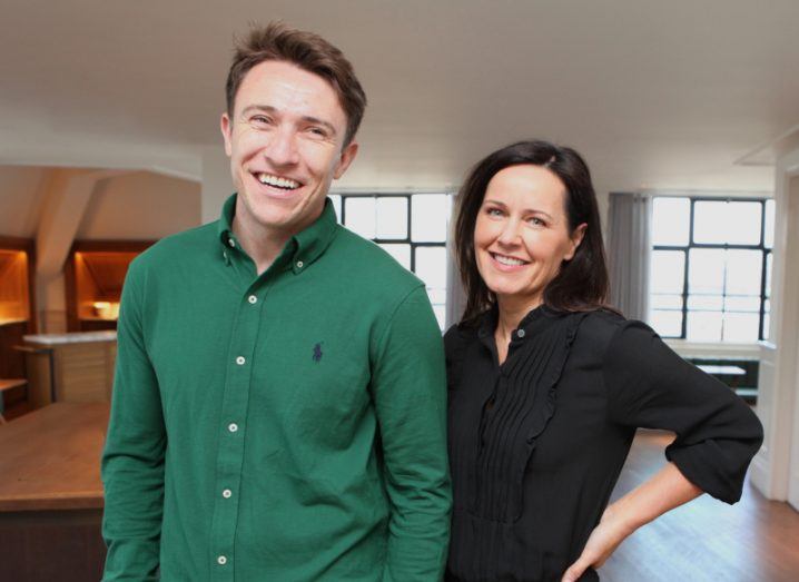 A man and a woman stand next to each other in a room and smile.