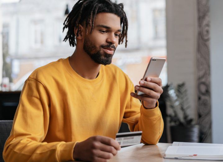 Man seated at a table stares at a smartphone in his hand.