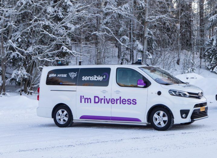 A white Toyota Proace van in snowy terrain with trees in the background. The vehicle has the Sensible 4 logo and "I'm Driverless" written on the side in purple letters, as the vehicle is using autonomous self-driving software.