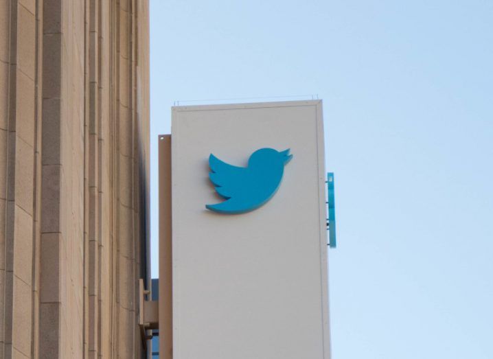 Twitter logo on a white billboard connected to a brown building, with a blue sky in the background.