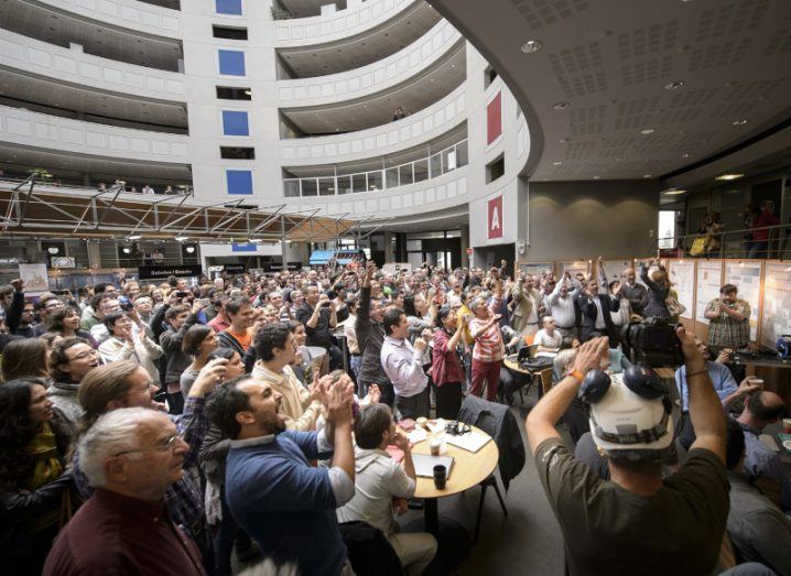 A large group of people celelbrating the Higgs boson achievement in a room at CERN.