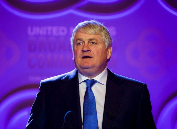 A man in a suit and tie speaking on a stage. He is Denis O'Brien, chair of Digicel Group.