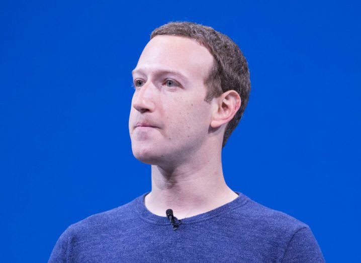 Meta CEO Mark Zuckerberg in a blue jumper looking out while on a stage with a blue background behind him.