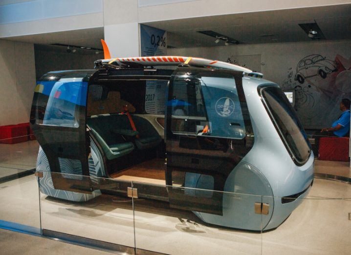 A concept of a self-driving vehicle showcased in the middle of a large room. The vehicle is displayed as an exhibit.