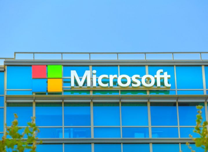 A building with the Microsoft logo on it, with some trees visible at the bottom sides of the image and a blue sky overhead.